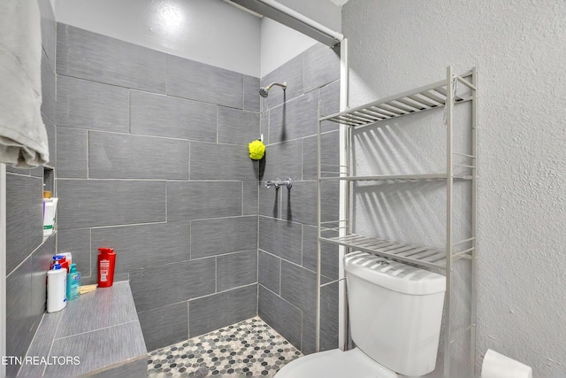 full bathroom featuring tiled shower, toilet, and a textured wall