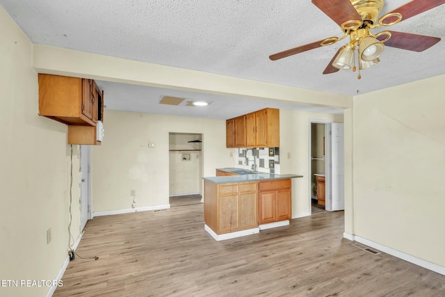 kitchen featuring light wood-type flooring, a peninsula, a ceiling fan, and visible vents