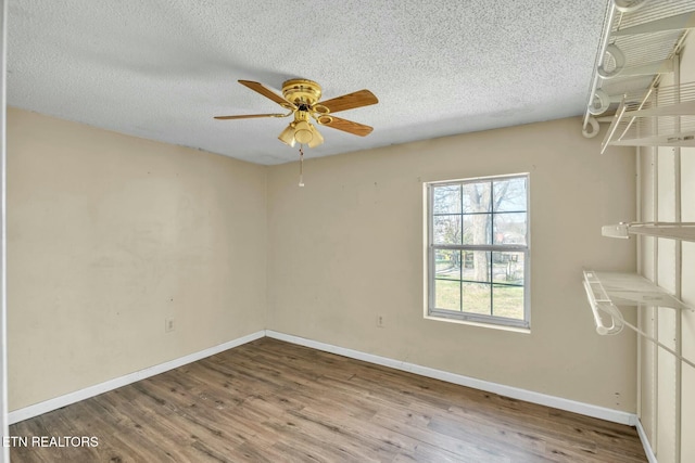 spare room featuring baseboards, wood finished floors, a textured ceiling, and ceiling fan