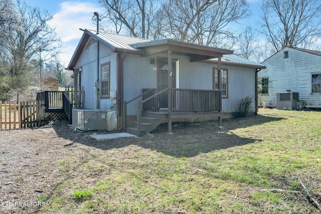 view of front of property featuring metal roof, central AC unit, a front lawn, and fence