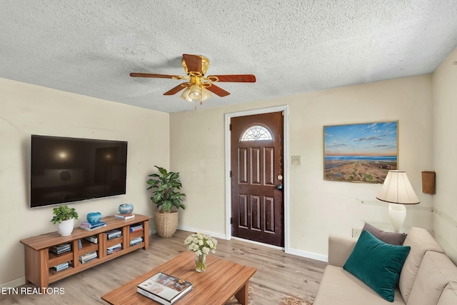 living room with a ceiling fan, light wood-style floors, baseboards, and a textured ceiling