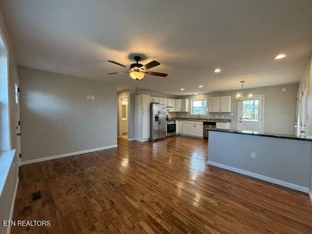 unfurnished living room with visible vents, dark wood-type flooring, ceiling fan with notable chandelier, recessed lighting, and baseboards