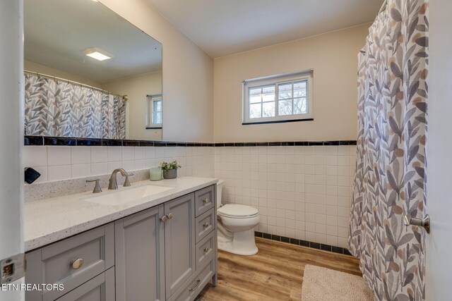 full bathroom with tile walls, toilet, wood finished floors, vanity, and wainscoting