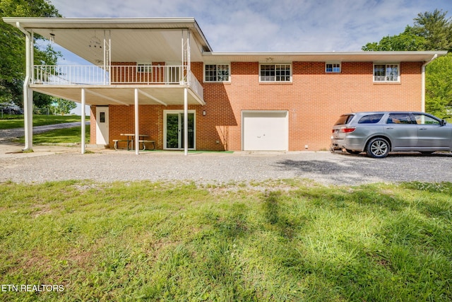 back of house with a lawn, brick siding, a garage, and gravel driveway
