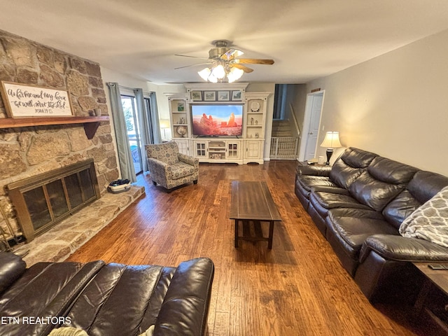 living area with stairs, a stone fireplace, wood finished floors, and a ceiling fan