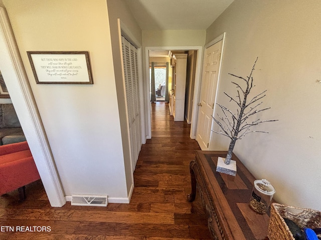 corridor featuring visible vents, baseboards, and wood finished floors