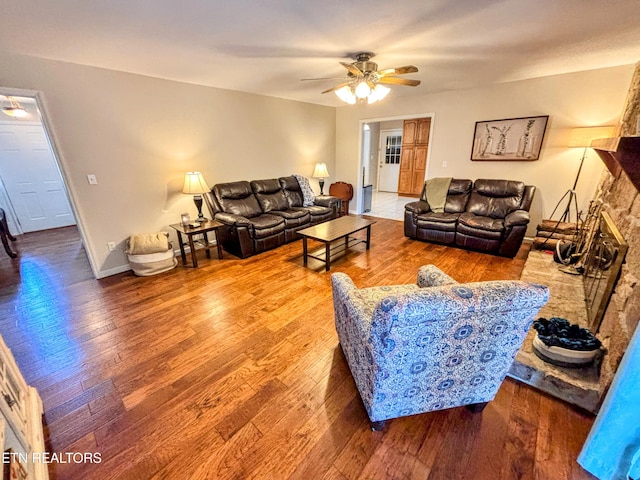 living room with baseboards, a large fireplace, a ceiling fan, and wood finished floors