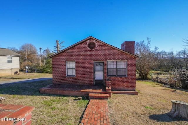 bungalow featuring brick siding, a chimney, and a front lawn