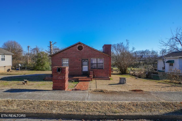 bungalow-style home featuring a front yard, brick siding, and a chimney