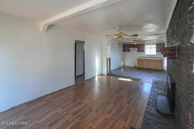 unfurnished living room featuring dark wood finished floors, beam ceiling, a textured ceiling, and ceiling fan