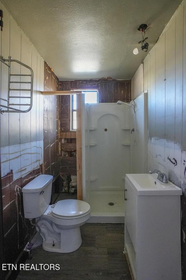 bathroom featuring wood finished floors, a stall shower, a sink, a textured ceiling, and toilet