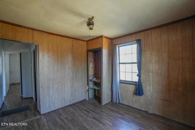 unfurnished bedroom with ornamental molding, wood walls, and wood finished floors