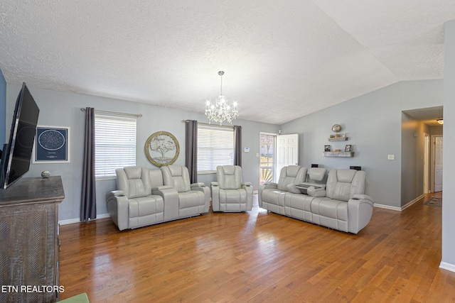 living area with a textured ceiling, wood-type flooring, baseboards, a chandelier, and vaulted ceiling