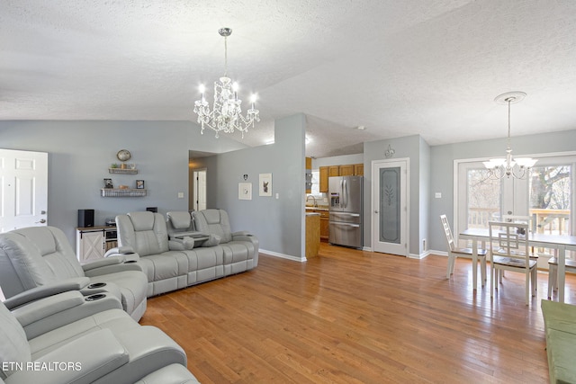 living room with baseboards, light wood-type flooring, lofted ceiling, an inviting chandelier, and a textured ceiling