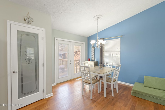 dining space featuring a textured ceiling, french doors, wood-type flooring, a chandelier, and vaulted ceiling