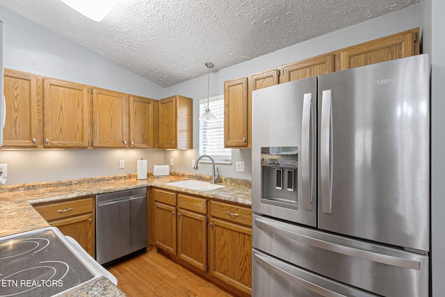 kitchen featuring light wood finished floors, light countertops, lofted ceiling, appliances with stainless steel finishes, and a sink