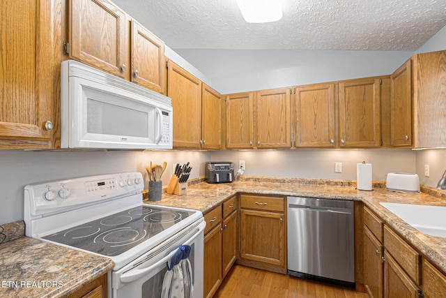 kitchen featuring a textured ceiling, white appliances, light wood-style floors, brown cabinetry, and lofted ceiling