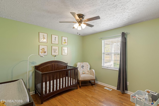 bedroom with visible vents, a crib, a textured ceiling, wood finished floors, and baseboards