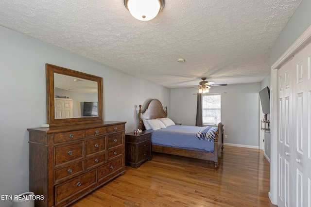 bedroom with ceiling fan, baseboards, light wood-type flooring, a closet, and a textured ceiling