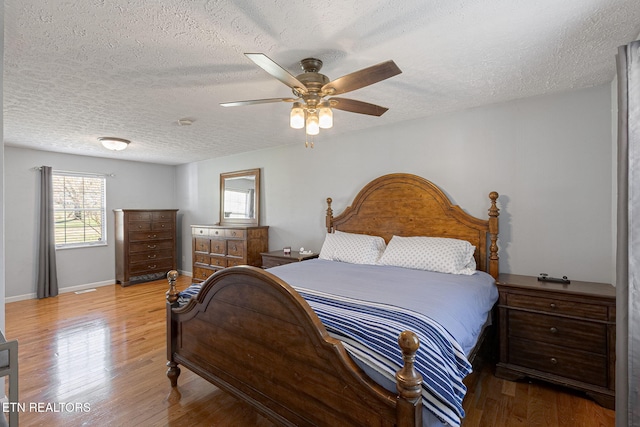 bedroom with a ceiling fan, wood finished floors, baseboards, and a textured ceiling