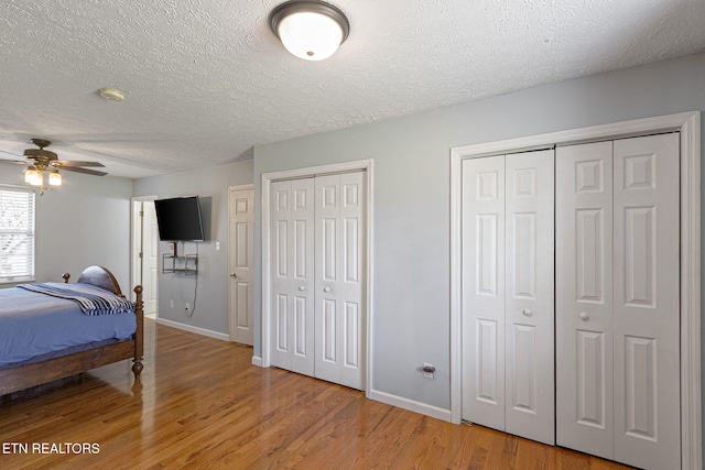 bedroom featuring light wood-style flooring, a textured ceiling, baseboards, and multiple closets