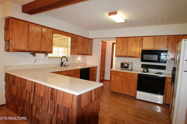 kitchen featuring a sink, black appliances, wood finished floors, and brown cabinetry