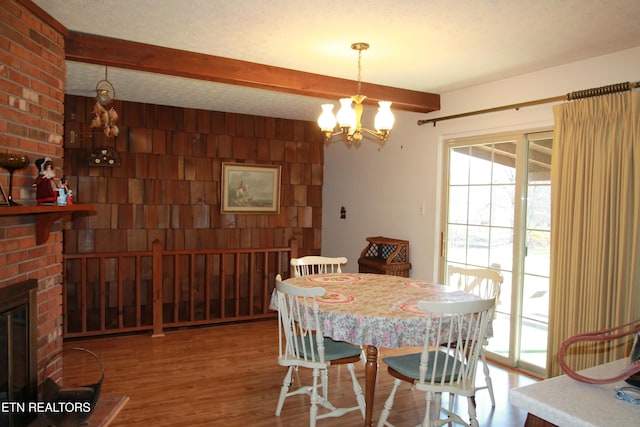 dining area featuring wood finished floors, beamed ceiling, an inviting chandelier, a textured ceiling, and a brick fireplace