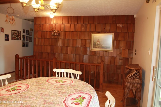 dining area featuring a textured ceiling, wood walls, and a chandelier