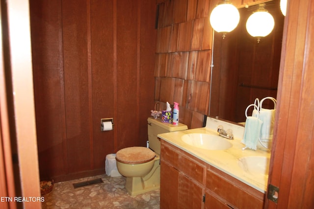 bathroom featuring wooden walls, visible vents, double vanity, a sink, and toilet