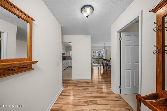 hall with light wood finished floors, a textured ceiling, and baseboards