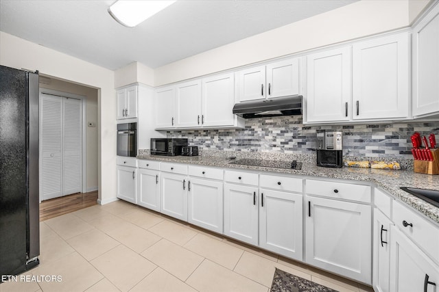 kitchen with under cabinet range hood, white cabinets, black appliances, and tasteful backsplash