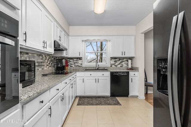 kitchen with under cabinet range hood, light stone counters, white cabinets, black appliances, and a sink