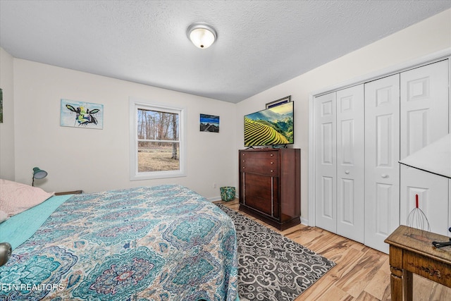 bedroom featuring a closet, light wood-style flooring, a textured ceiling, and baseboards