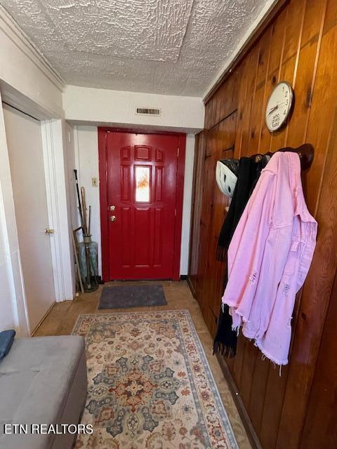 entrance foyer with visible vents, wooden walls, and a textured ceiling