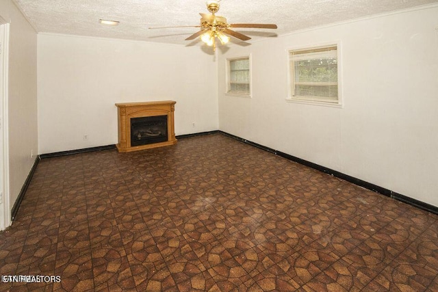 unfurnished living room with stone finish flooring, baseboards, ceiling fan, a fireplace, and a textured ceiling