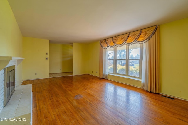 unfurnished living room with light wood-type flooring, visible vents, and a fireplace