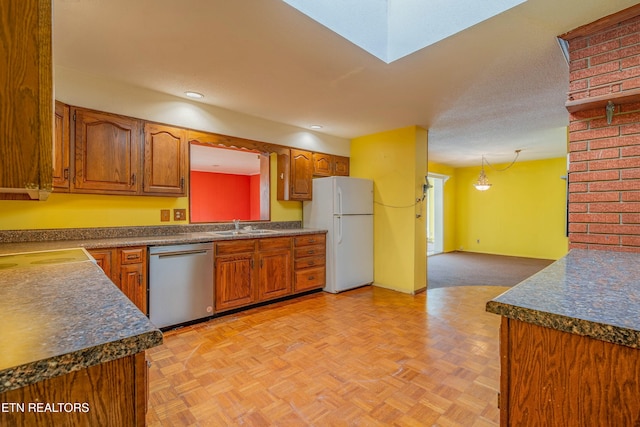 kitchen with dark countertops, a sink, freestanding refrigerator, and stainless steel dishwasher