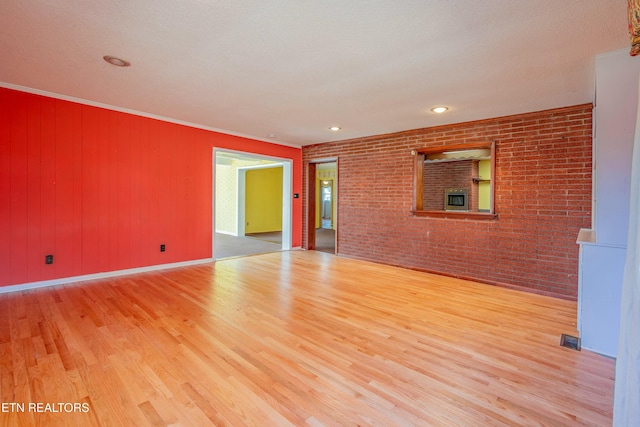 spare room featuring wood finished floors, visible vents, brick wall, and ornamental molding