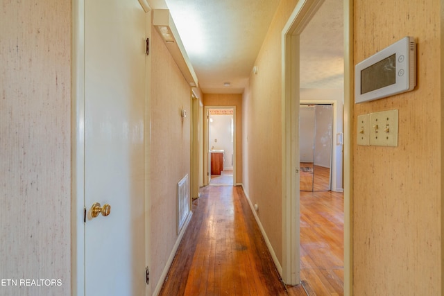 corridor featuring visible vents, baseboards, and hardwood / wood-style flooring