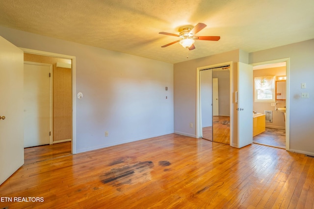 unfurnished bedroom with a ceiling fan, baseboards, ensuite bath, a textured ceiling, and light wood-type flooring