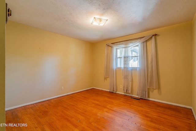 spare room with light wood-type flooring, visible vents, and baseboards