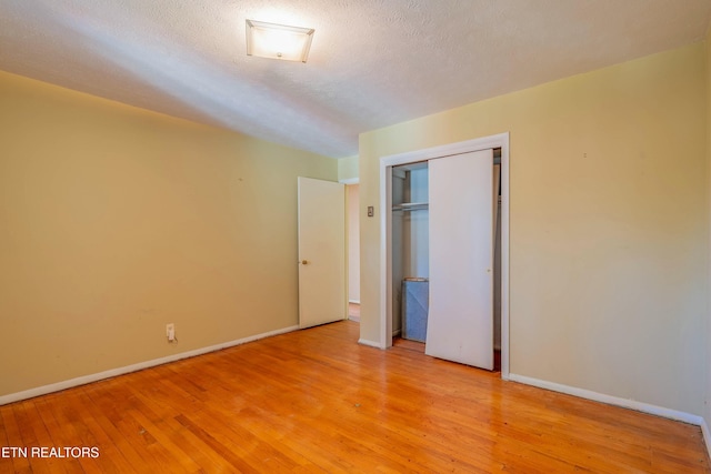 unfurnished bedroom with baseboards, a closet, light wood finished floors, and a textured ceiling