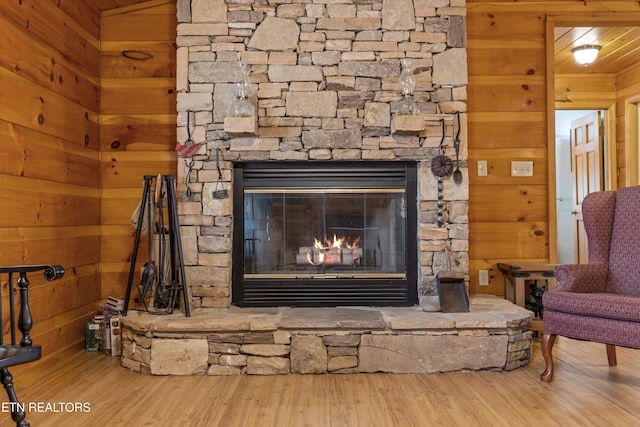 room details featuring a stone fireplace, wooden walls, and wood finished floors