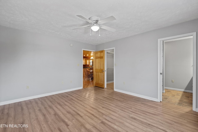 unfurnished bedroom with a walk in closet, baseboards, light wood-type flooring, a textured ceiling, and a ceiling fan