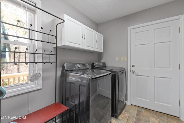 washroom with washer and dryer, a textured ceiling, cabinet space, and stone finish flooring