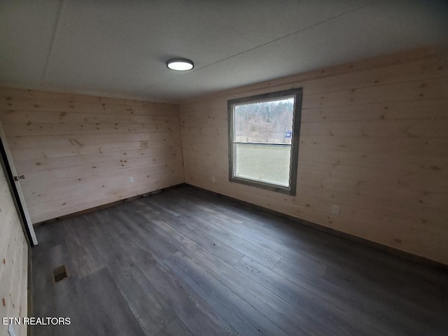 empty room featuring dark wood finished floors, wooden walls, and visible vents