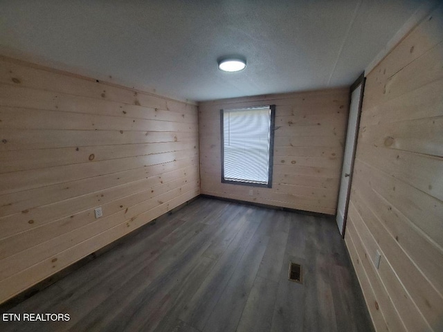 empty room featuring visible vents, wood finished floors, and wood walls