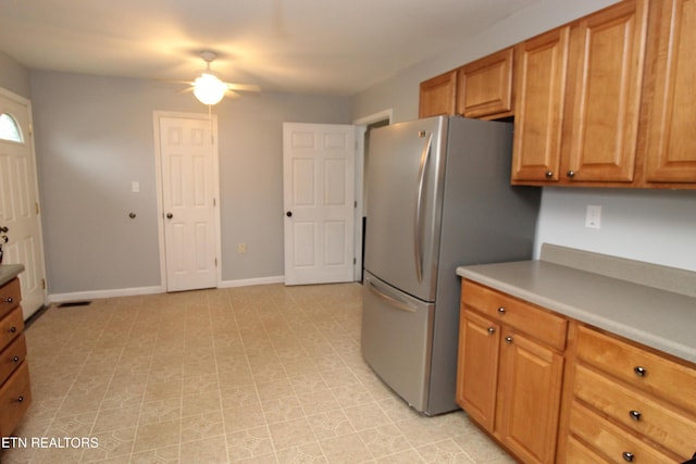 kitchen with a ceiling fan, freestanding refrigerator, brown cabinetry, light countertops, and baseboards