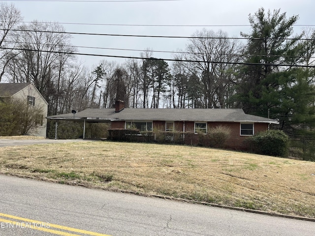 single story home featuring brick siding, driveway, a chimney, and a front lawn