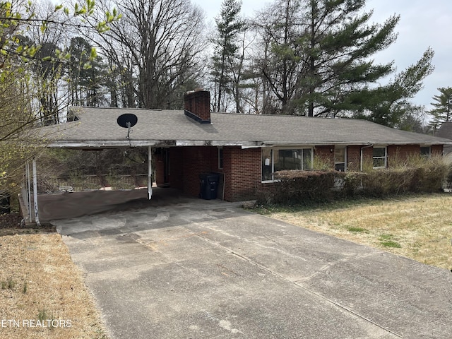 ranch-style home featuring brick siding, an attached carport, a shingled roof, a chimney, and driveway